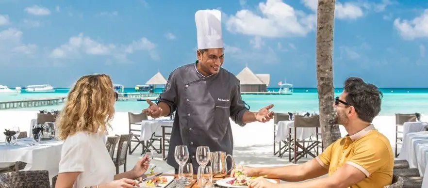 A resort chef talking a couple through a beachside lunch