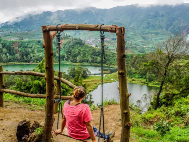 Traveller on a swing overlooking a lake in the Dieng highlands
